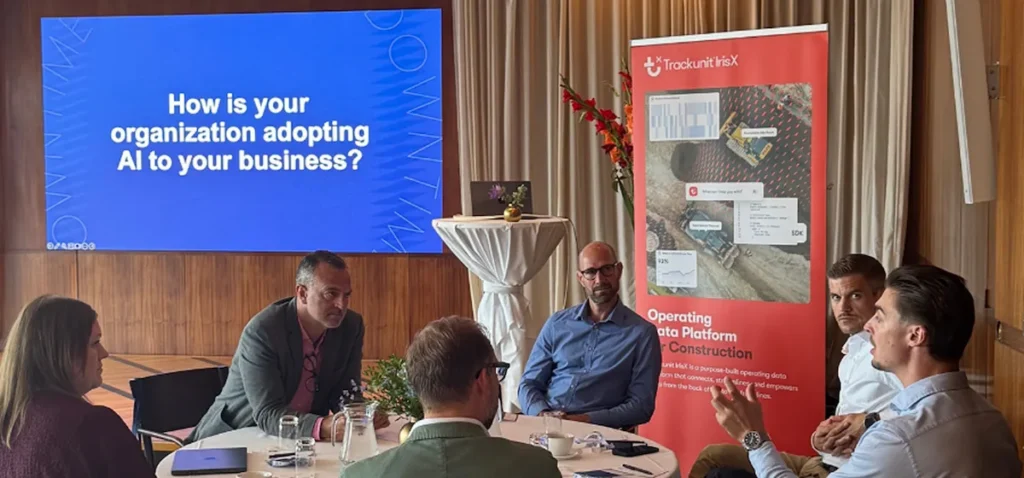 A group of people sitting at a meeting room table in front of a presentation screen and a banner for a construction IoT data platform focused on AI in the Nordics.