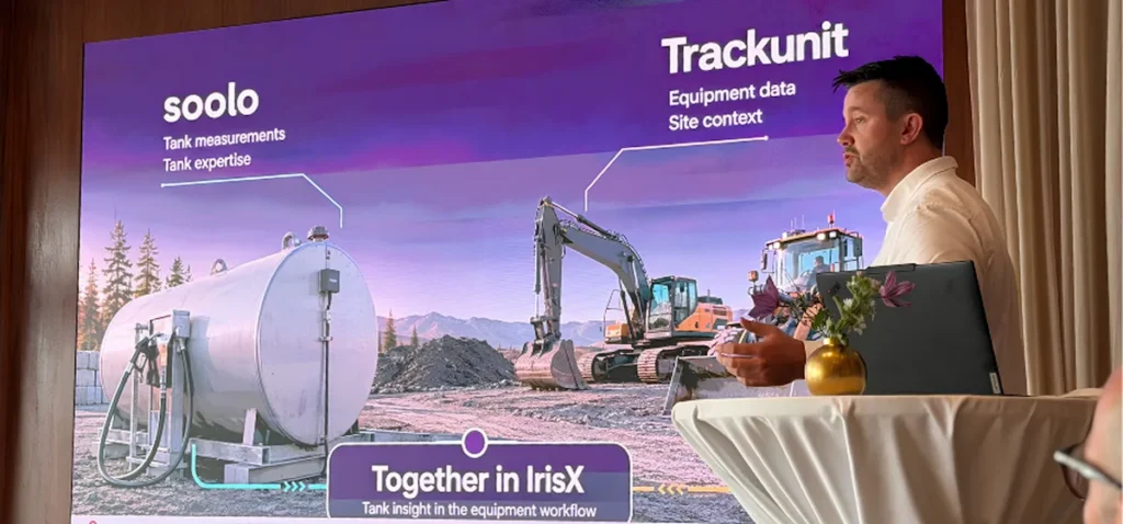 A presenter at a podium in front of a screen displaying AI analytics for tank measurements and site data on a connected jobsite in the Nordics.
