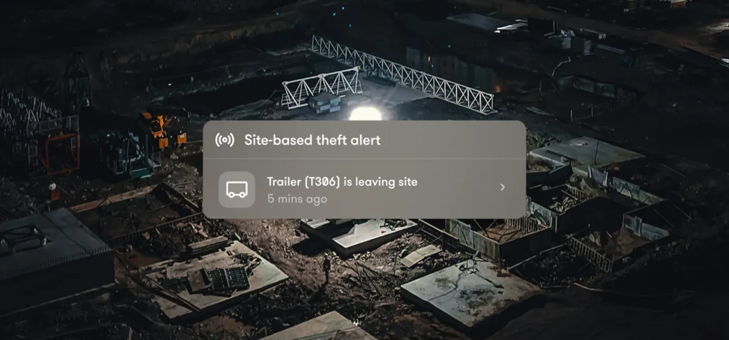 Aerial view of a construction site at night with a construction equipment tracking notification indicating a trailer is leaving the area.