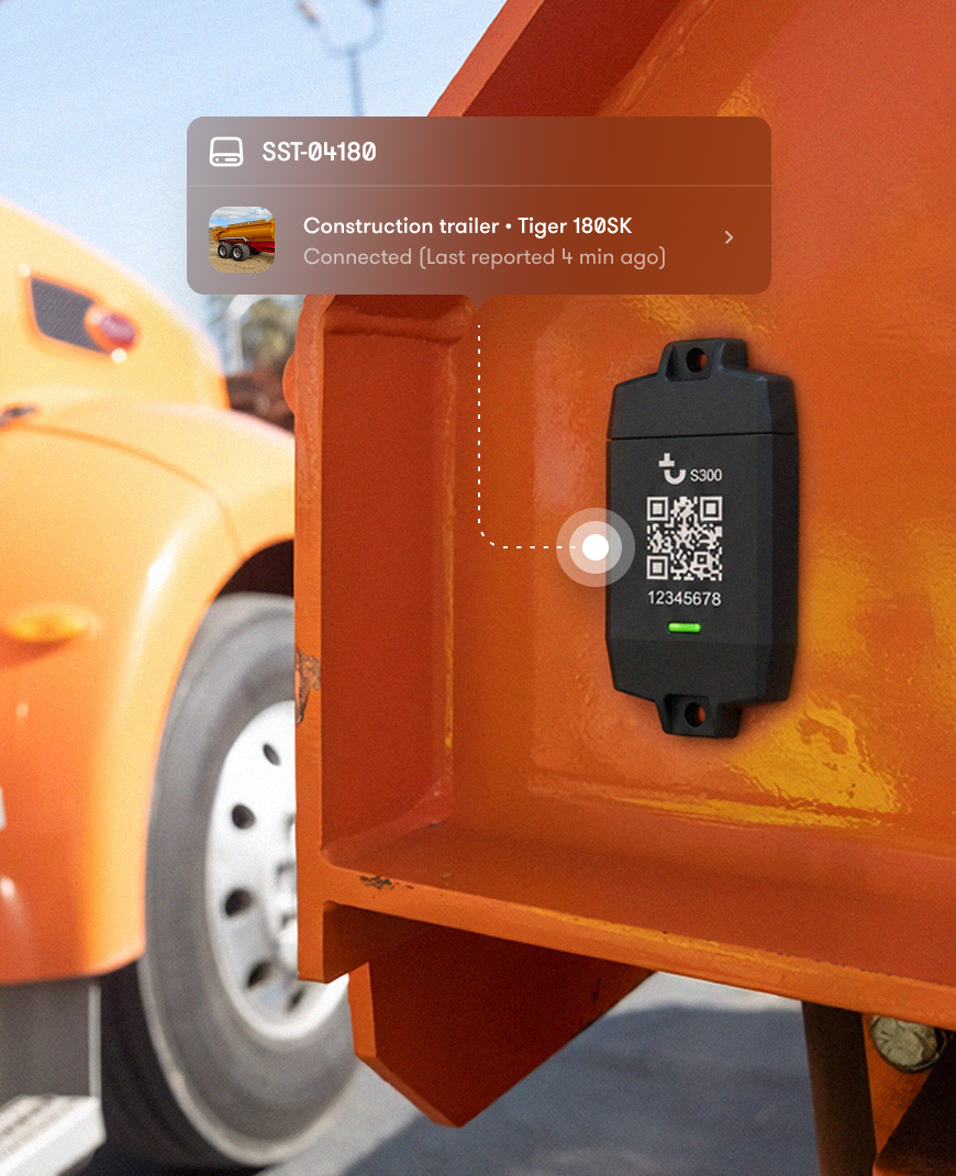 Close-up of a black tracking device with QR code on orange construction equipment, showing a digital overlay of status and connection details, with an orange truck in the background. Construction equipment tracking.