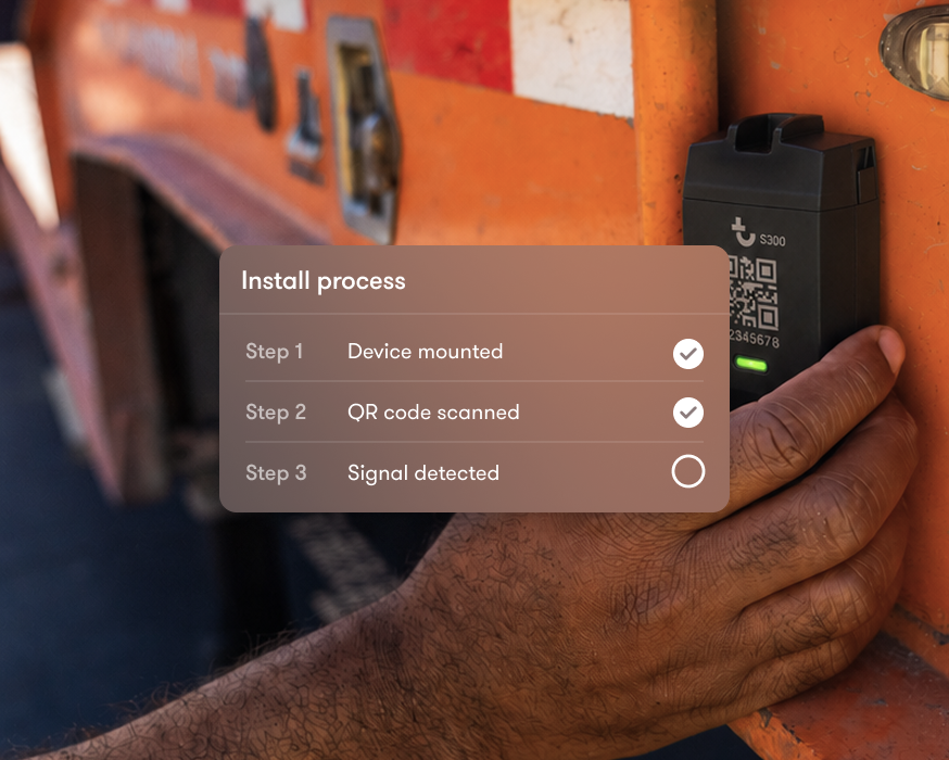 A hand holds a mounted device on an orange vehicle, with an overlay showing installation steps for construction equipment tracking: Device mounted and QR code scanned are checked, but Signal detected is unchecked.