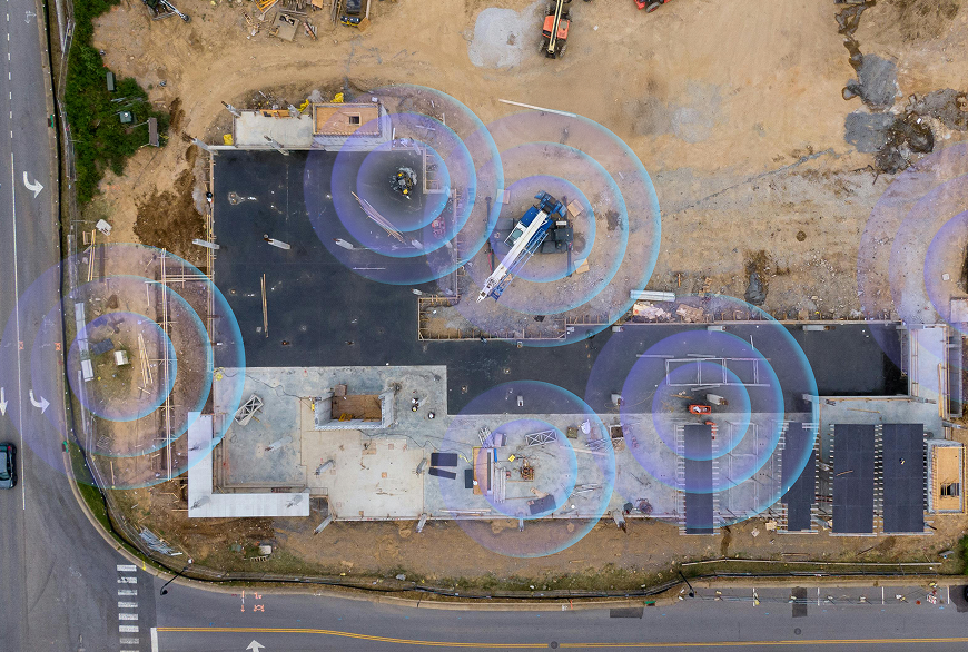Aerial view of a construction site with digital blue circles highlighting construction IoT integration around the building and equipment.