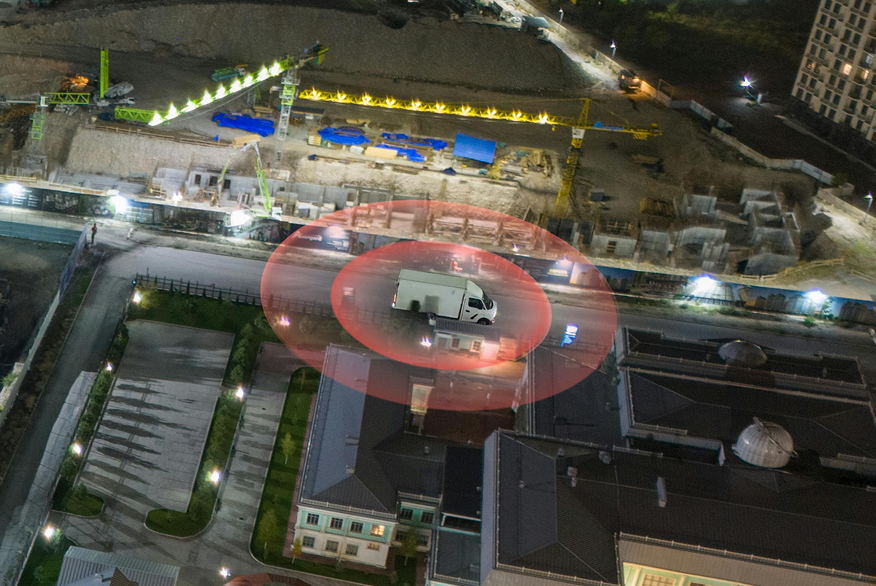 A white van is parked at night within a red radar-like circle, with cranes and a construction site in the background, illustrating construction equipment tracking.