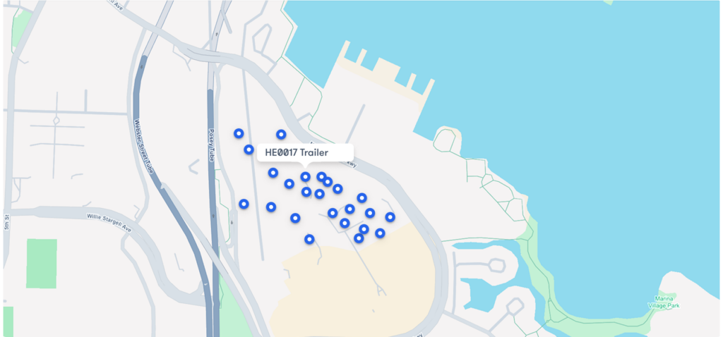A map displays clustered blue markers around a labeled point, HED017 Trailer, next to a body of water and several roads, highlighting construction equipment tracking.