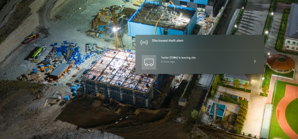 Aerial night view of a construction site with a security alert overlay indicating a trailer is leaving. The site and nearby sports track are brightly lit. Unpowered asset tracking rental solutions help monitor equipment and trailers, supporting construction equipment tracking after hours.