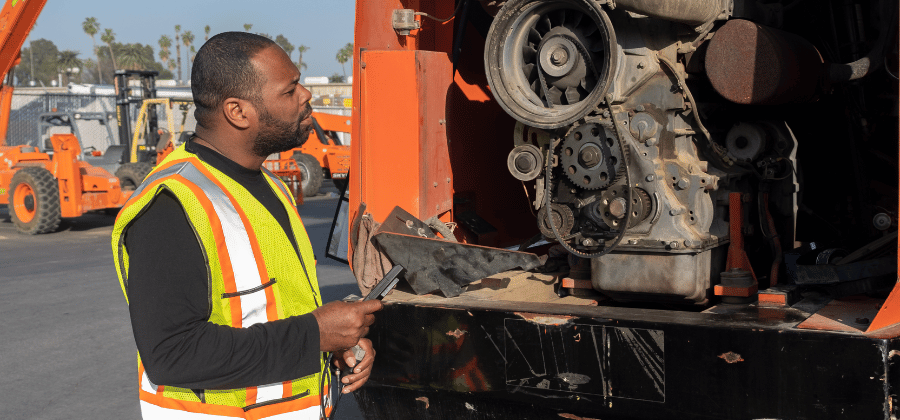 A technician in a safety vest connects a diagnostic tool to a construction machine's engine.