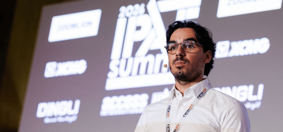 A man with glasses stands on stage at the 2024 IPAF Summit in front of a projection screen at a connected jobsite.