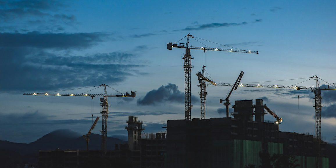 Tower cranes silhouetted against a cloudy sky at a connected jobsite where eliminating downtime still depends on trust.