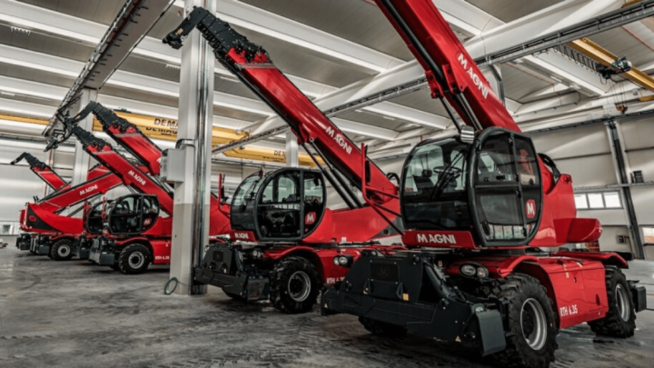 Large red telescopic handlers with extended arms line up in a well-lit warehouse, ready for use or maintenance. Fleet management.