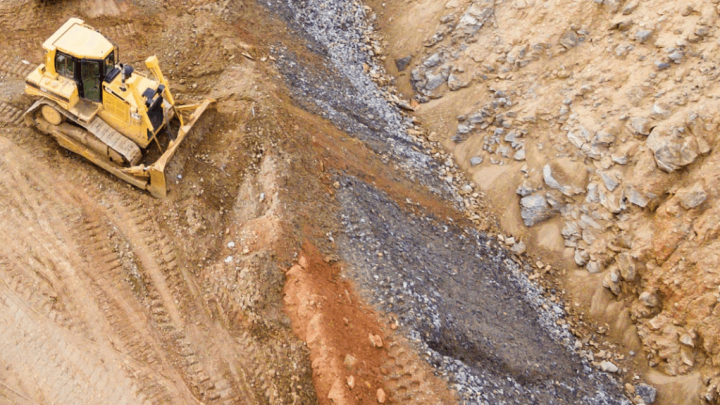 A yellow bulldozer levels earth on a rocky, sandy construction site with loose gravel, supporting a connected jobsite project.