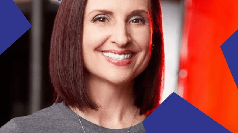 Smiling woman with shoulder-length brown hair in a gray t-shirt, standing before blue geometric shapes, representing connected jobsite.