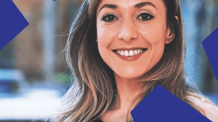 A woman with long brown hair smiles outdoors, with large blue geometric shapes in the corners, relating to connected jobsite.