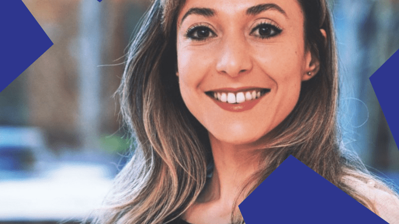 A woman with long brown hair smiles outdoors, with large blue geometric shapes in the corners, relating to connected jobsite.