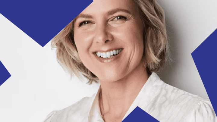 A smiling woman with short blonde hair in a white blouse, partly behind blue geometric shapes, representing connected jobsite.