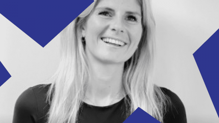 A woman with long blonde hair in a black top smiles at the camera. Black and white photo with blue shapes, hinting at connected jobsite.