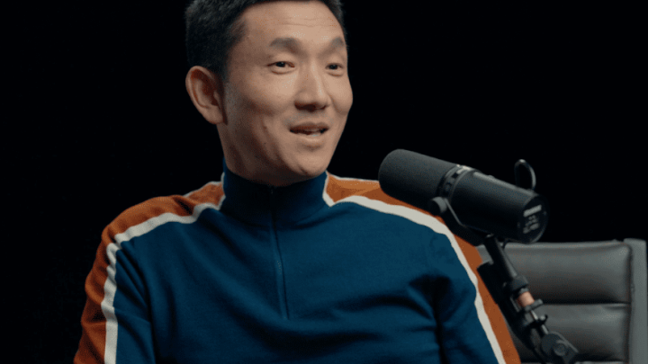 A man in a blue and orange striped sweater speaks into a microphone in a studio, discussing safe equipment access in fleet management.