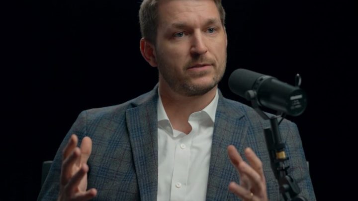A man in a plaid blazer and white shirt sits by a microphone, discussing safe equipment access for fleet management.