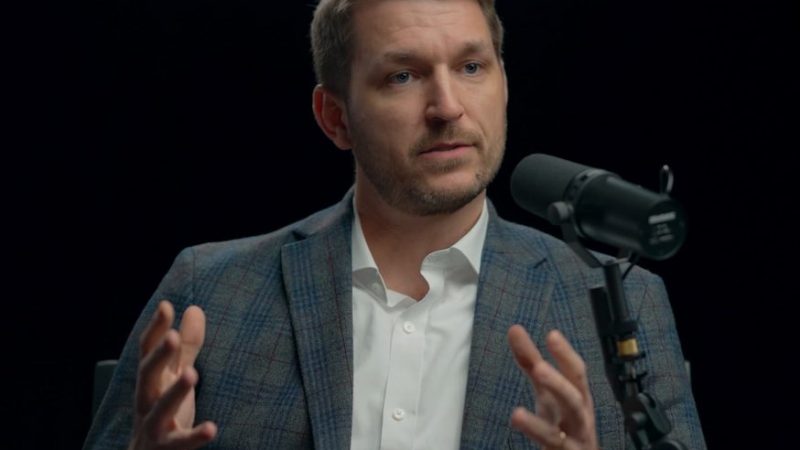 A man in a plaid blazer and white shirt sits by a microphone, discussing safe equipment access for fleet management.