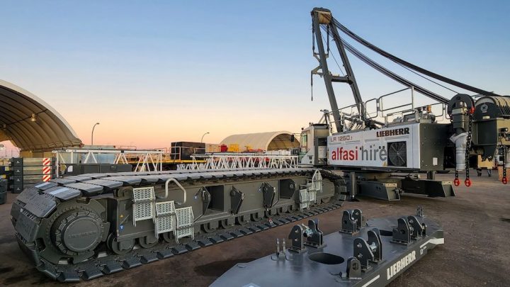 A large Liebherr crawler crane with detached treads sits on a construction site at sunset, highlighting construction equipment tracking.