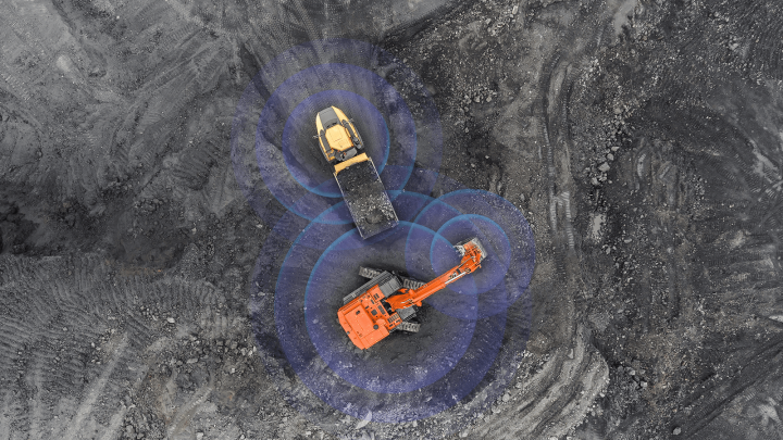 Aerial view of an excavator loading a dump truck at a construction site, with blue circles showing connected jobsite technology.