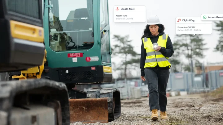 A worker in a high-visibility vest uses digital access management to unlock an excavator, illustrating connected jobsite technology.