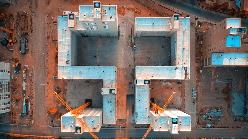 Aerial view of a construction site with two large buildings and yellow cranes, showing efficient connected jobsite coordination.