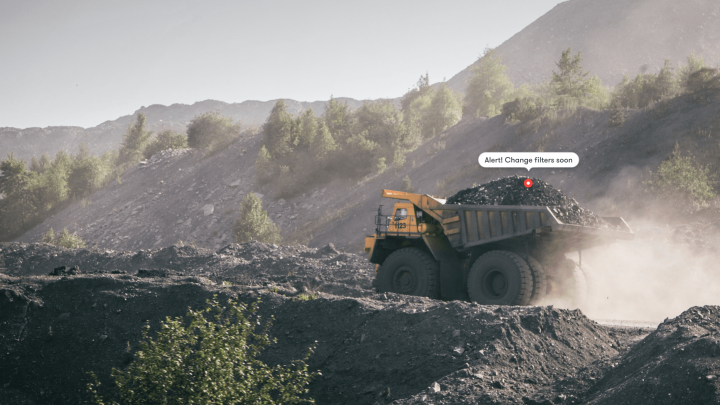 A mining dump truck hauls coal through dusty terrain as a Construction AI alert says, “Alert! Change filters soon.” Fleet management.