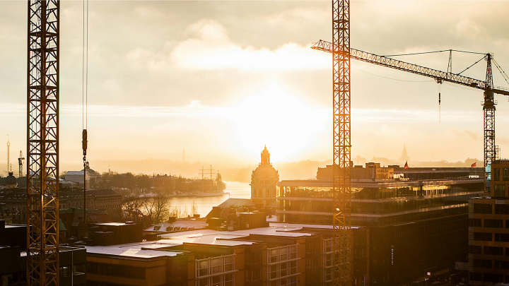 Sunrise over a cityscape with cranes, historic buildings, and a river, highlighting ongoing construction in Central and Eastern Europe supported by EU funding; an example of connected jobsite transformation.