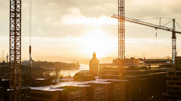 Two tall construction cranes overlook a city skyline at sunset on a connected jobsite in the Nordics.