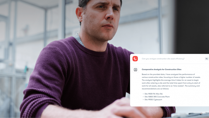 A man in a maroon sweater reviews a computer screen showing a construction site report and recommended installs, highlighting connected jobsite.