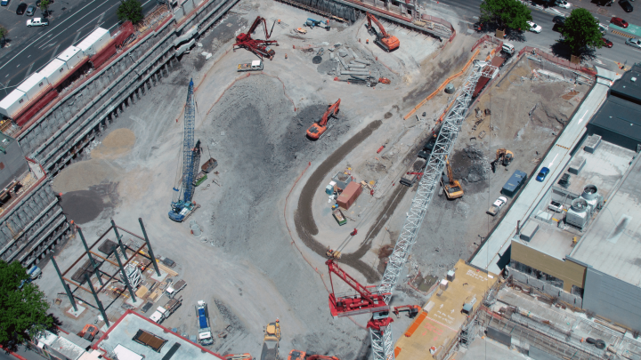 Aerial view of a construction site with cranes, excavators, vehicles, and materials; site shows partial excavation and connected jobsite.