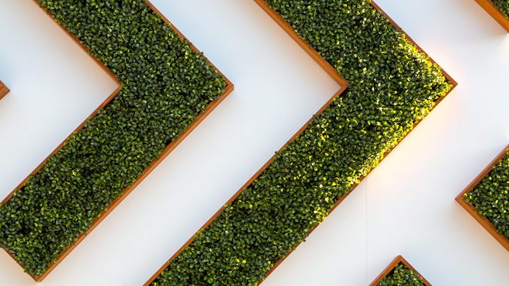 Trimmed green plants form zigzag patterns on a white wall, highlighting sustainable design and connected jobsite themes.