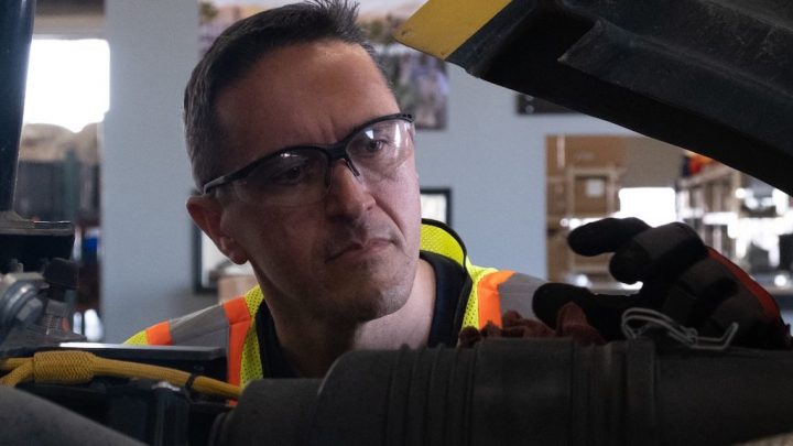A man in safety gear inspects machinery indoors, highlighting the role of fleet management in operational efficiency and safety.