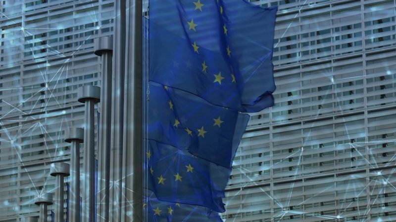 EU flags flutter before a modern glass building with a faint digital network overlay, reflecting policies for construction IoT progress.