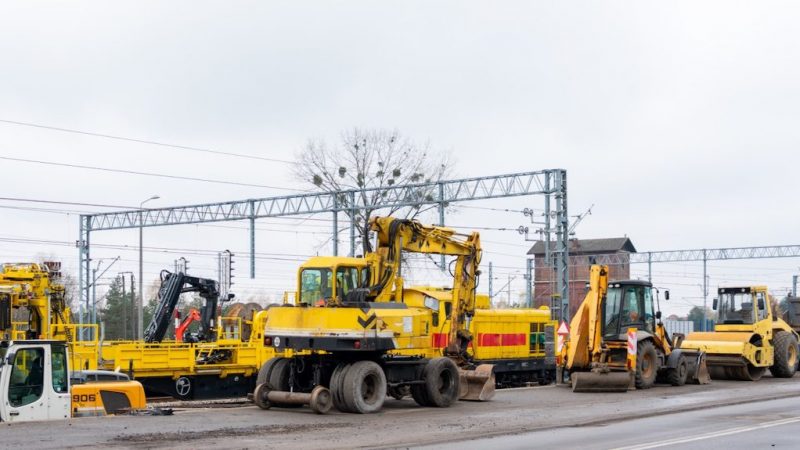 Yellow excavators, bulldozers, and rollers are parked by a road near tracks as workers coordinate construction fleet management.