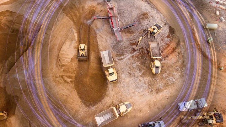 Aerial view of a construction site with yellow trucks and excavators moving dirt on curved tracks, highlighting fleet management.