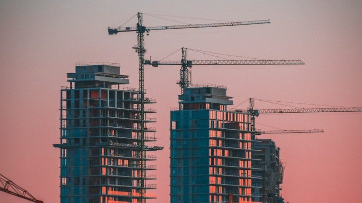 Silhouetted tall buildings and cranes under a pink-orange sunset sky, highlighting ambitious growth and connected jobsite progress.