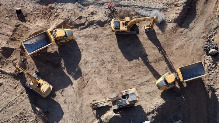 Aerial view of a construction site with four yellow excavators and dump trucks arranged in a circle, highlighting connected jobsite.