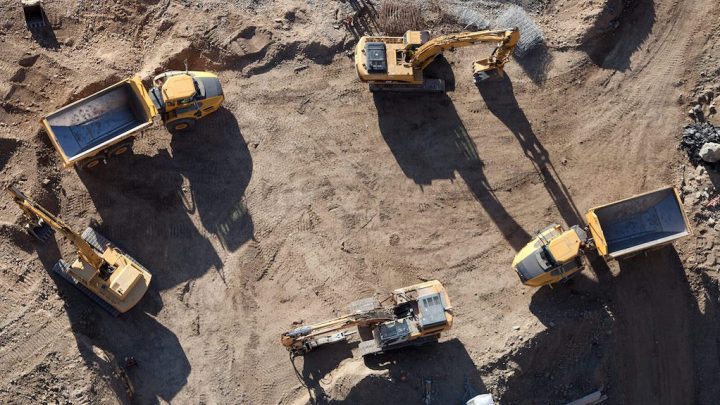 Aerial view of a construction site with excavators and dump trucks on dusty ground, showcasing connected jobsite technology.