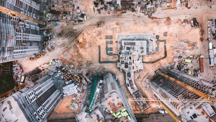 Aerial view of a Construction 4.0 site with cranes, high-rise buildings in progress, vehicles, and sandy ground, showing a connected jobsite.