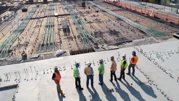 Six construction workers in safety gear discuss Big Data at a construction site, highlighting the connected jobsite environment.