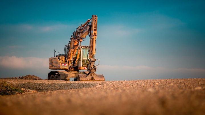 A large yellow excavator gathers data on a gravel site under blue sky, with dirt and rocks behind, showcasing construction telematics.