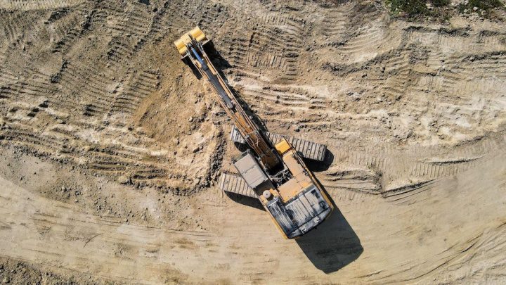 Aerial view of a yellow excavator on a construction site with tire and track marks in the dirt, illustrating telematics.
