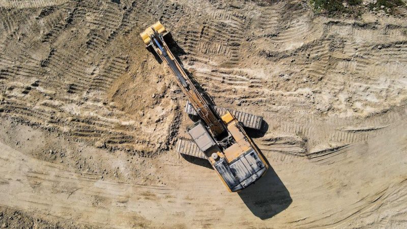 Aerial view of a yellow excavator on a construction site with tire and track marks in the dirt, illustrating telematics.