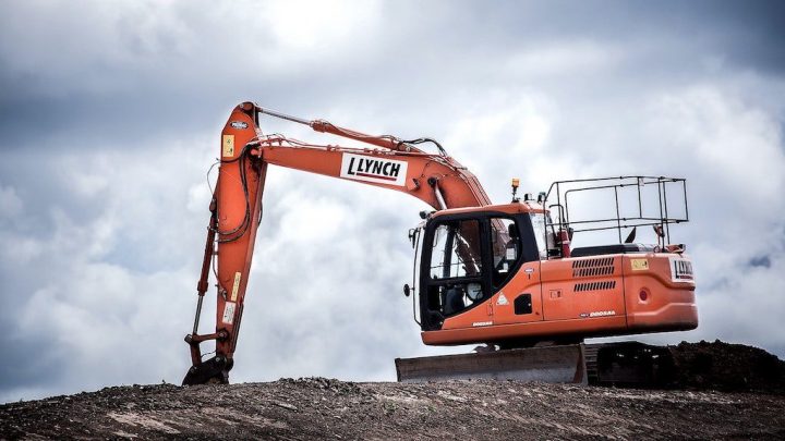 An orange LYNCH excavator sits on a dirt mound under a cloudy sky, demonstrating durable construction equipment.