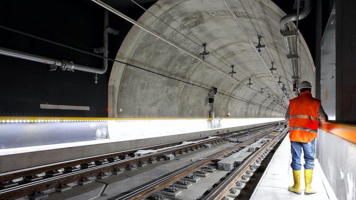 A worker in safety gear stands on a walkway in a modern railway tunnel with IoT-connected overhead lines, showing a connected jobsite.