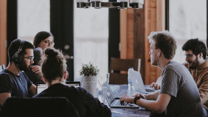 Five people collaborate on laptops in a bright, modern workspace, suggesting a connected jobsite environment.