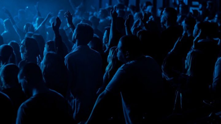 A blue-lit concert crowd enjoys seamless music transitions, eliminating downtime like connected jobsites streamline construction.