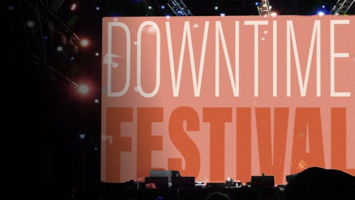 A large stage screen reading DOWNTIME FESTIVAL is framed by lights and gear, capturing the energy of a connected jobsite event.