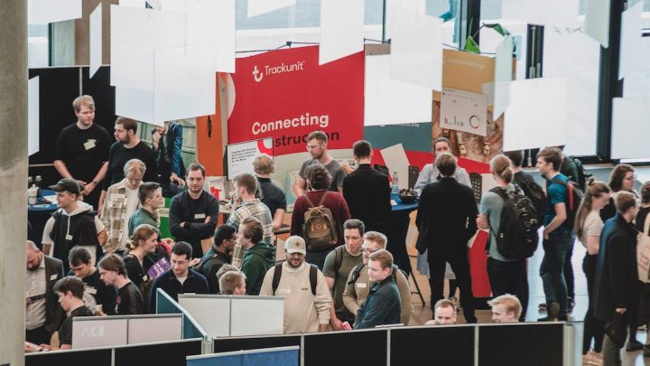 Crowd at a busy indoor event with red and yellow booths, exploring Internet of Things displays for construction IoT solutions.